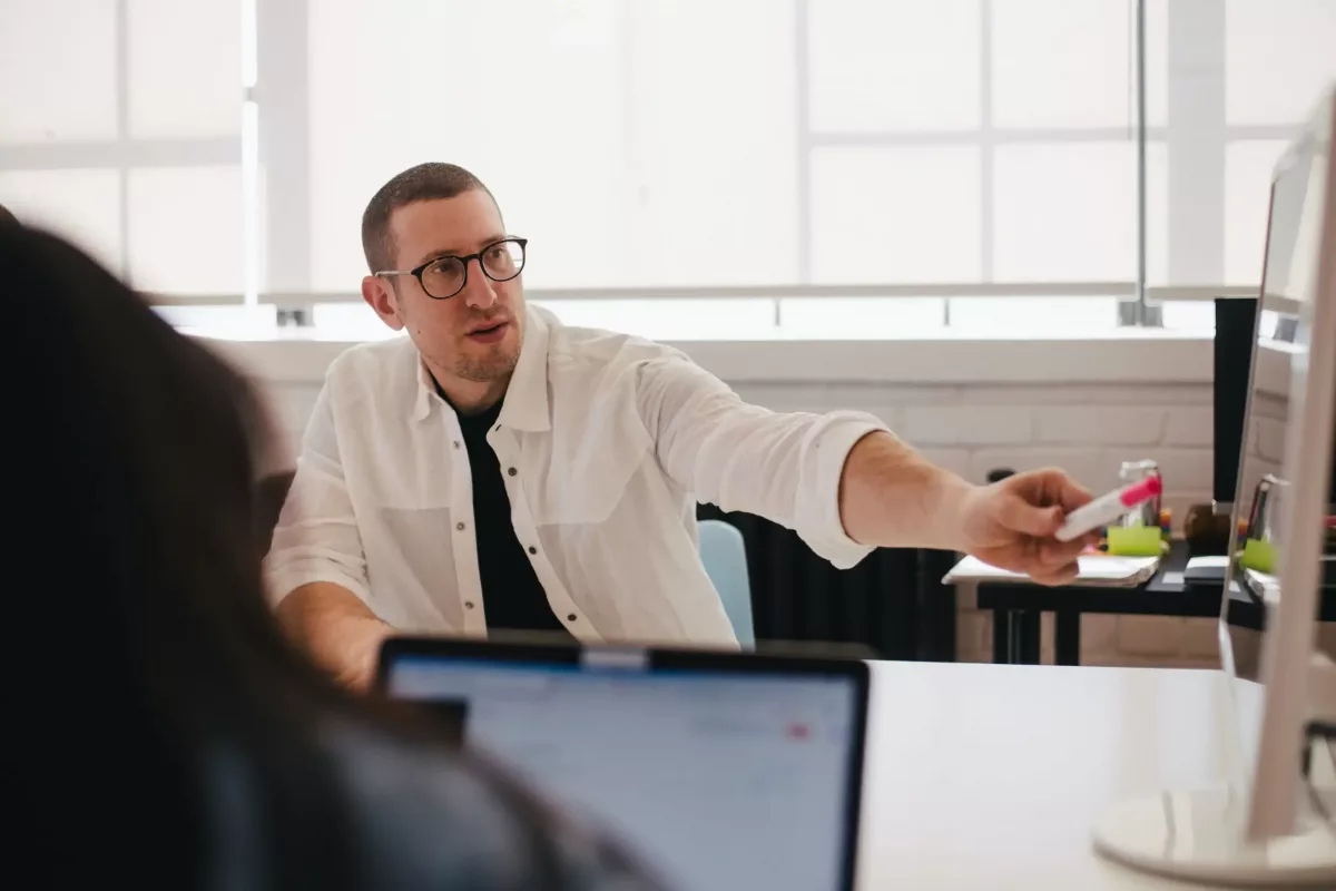 Homme avec des lunettes et une chemise blanche, pointant du doigt hors-cadre